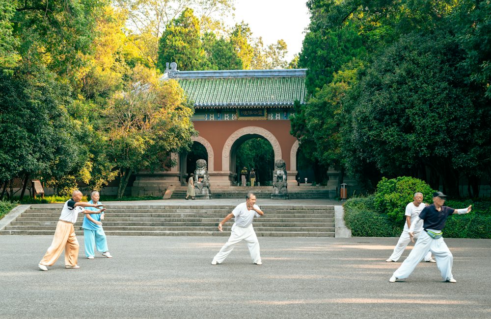 People practising tai chi in a park in front of a traditional Chinese gateway